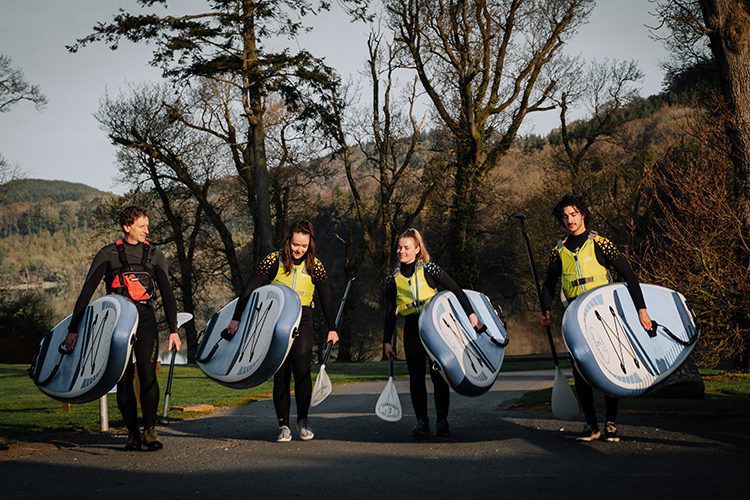 four people carrying their stand up paddle boards