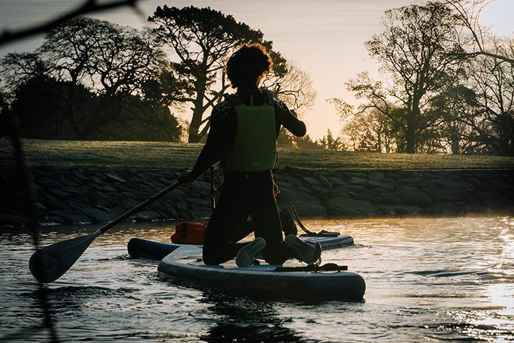 Man kneeling on paddle board in early morning sunrise on castlewellan lake