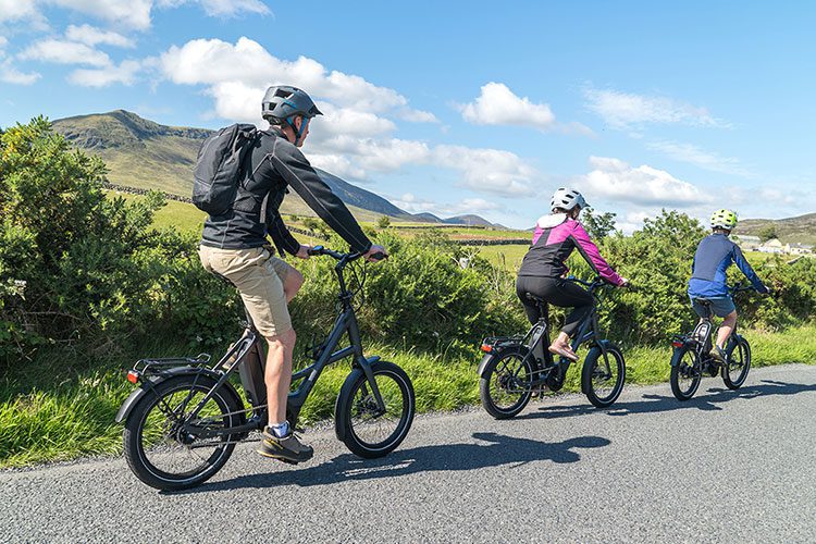 Three family members cycling along a main road near Slieve Muck inside the Kingdom of Mourne